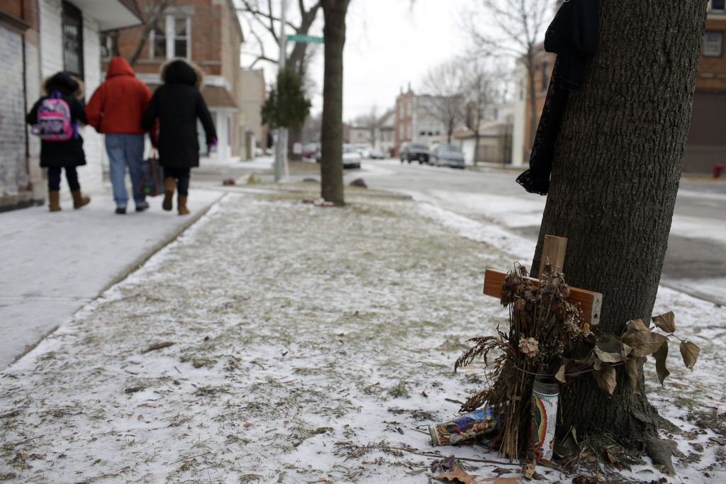 People walk past a makeshift memorial where a person was killed next to a tree January 13, 2017 in Chicago, Illinois. Ceasefire violence interrupters try and prevent violent crimes such as shootings before they happen by communicating with residents in the neighborhood, gang members and relatives of gang members. (Photo by Joshua Lott for The Trace)