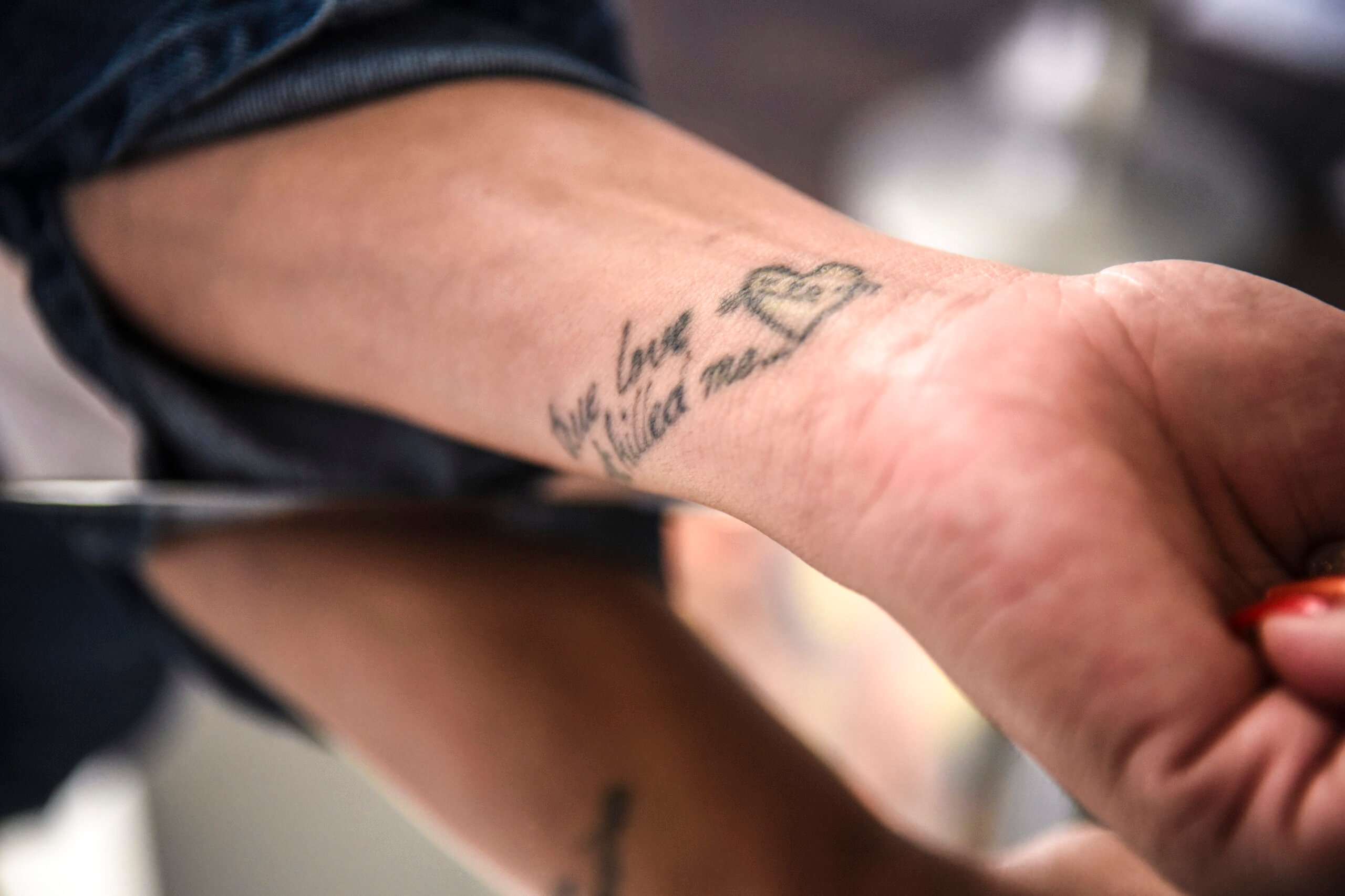 A person's forearm above a mirrored table, with a tattoo that reads "True love almost killed me."