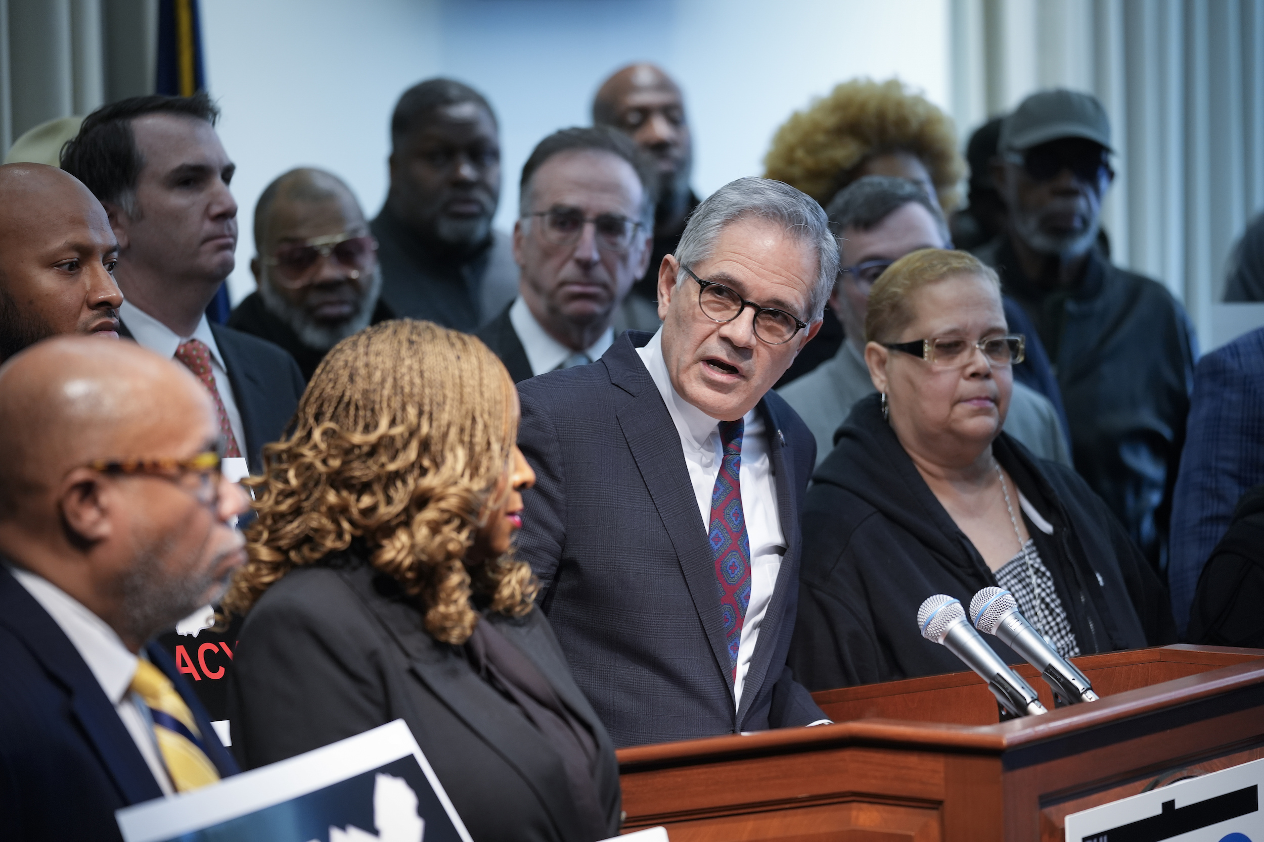 A few Philadelphia officials, including Larry Krasner, stand at a podium with two microphones.
